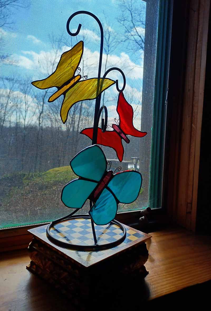 Three stained glass butterflies on a hooked stand in a window.