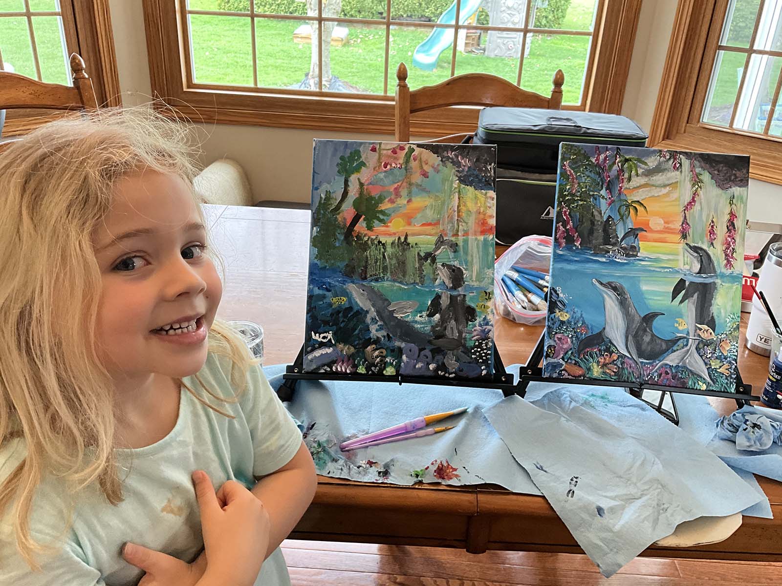 Child sitting with paintings she just painted.