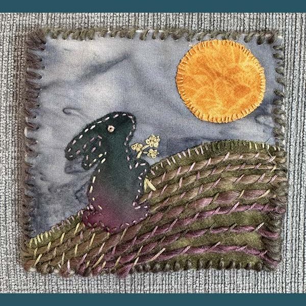 Handstitched scene of a rabbit in a field under the sun.