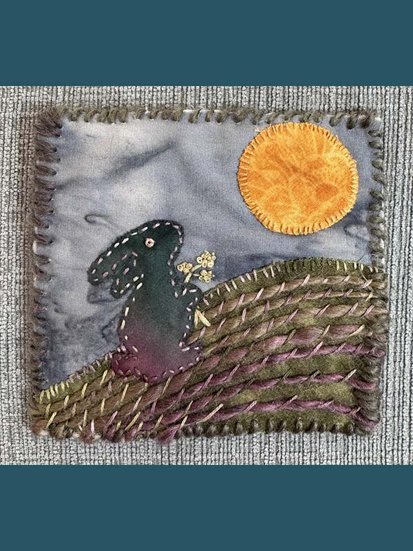 Handstitched scene of a rabbit in a field under the sun.