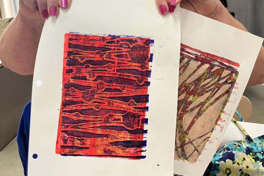 Adult holding two samples of mono prints she created using Gelli plates.