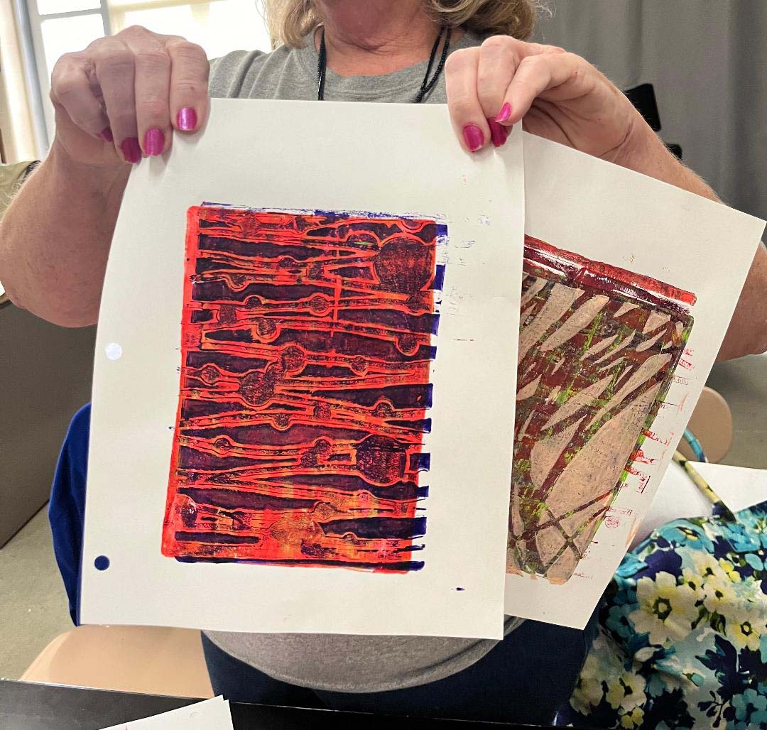 Adult holding two samples of mono prints she created using Gelli plates.