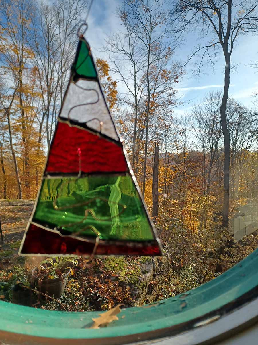 Red, white and green stained glass Christmas Tree ornament hanging in window.