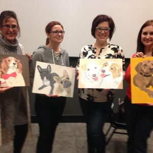 Four women posing with paintings they created of their pets.